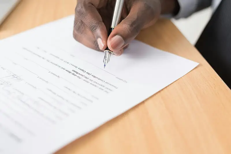 Mão assinando um documento impresso sobre a mesa.